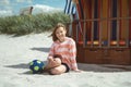 Cute little girl sitting on white sand with ball on beautiful beach with dunes on Baltic sea Royalty Free Stock Photo