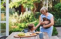 Cute little girl sittting at table and having breakfast in garden of country house and petting cat Royalty Free Stock Photo