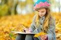 Cute little girl sketching outside on beautiful autumn day. Happy child playing in autumn park. Kid drawing with colourful pencils Royalty Free Stock Photo