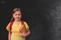 Little girl smiling and holding a book and   standing against empty blackboard with place for text Royalty Free Stock Photo