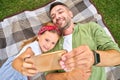 Cute little girl spending time with her father, taking selfie using smartphone while lying down on a blanket in the Royalty Free Stock Photo