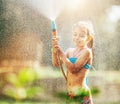 Cute little girl sprinkls a water for herself from the hose, makes a rain. pleasure for hot summer days