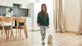 A cute little girl standing in a middle of a kitchen holding a leash of her white toy dog Royalty Free Stock Photo