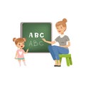 Cute little girl standing near the blackboard and writing letters of the English alphabet, teacher helping her, language Royalty Free Stock Photo