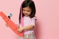 a cute little girl is standing on a pink background in a pink T-shirt, holding her skate in her hands, looking at it Royalty Free Stock Photo