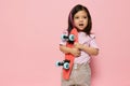 a cute little girl is standing on a pink background in a pink T-shirt, holding her skate in her hands, looking at it Royalty Free Stock Photo