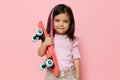 a cute little girl is standing on a pink background in a pink T-shirt, holding her skate in her hands, looking at it Royalty Free Stock Photo