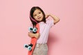 a cute little girl is standing on a pink background in a pink T-shirt, holding her skate in one hand in front of her Royalty Free Stock Photo
