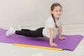 cute little girl stands in a plank on a mat, a gymnastic stick lies nearby, the child smiles Royalty Free Stock Photo