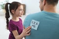 Cute little girl sticking note with words Kick Me to father`s back at home