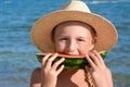 Cute little girl in straw hat eating juicy watermelon on beach, closeup Royalty Free Stock Photo