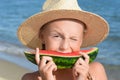 Cute little girl in straw hat eating juicy watermelon on beach, closeup Royalty Free Stock Photo