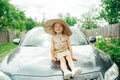 Cute little girl in straw hat sitting on car hood in village Royalty Free Stock Photo