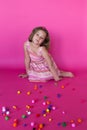 Cute little girl in summer dress sitting behind scattered colorful pompoms