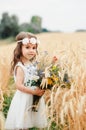 Cute little girl in the summer field of wheat. A child with a bouquet of wildflowers in his hands