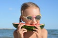 Cute little girl with sunglasses eating juicy watermelon on beach, closeup Royalty Free Stock Photo