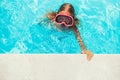 Cute little girl swims in the pool wearing diving goggles, Child smiles and looks at the camera, Happy child plays in the pool