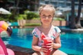 Cute little girl in swimsuit sitting near swimming pool with inflatable pink flamingo and drinking fresh watermelon juice. Summer Royalty Free Stock Photo