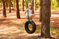 Cute little girl swinging on wheel attached to big tree in forest.