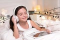 Little girl with tablet listening to music through headphones in bed at home Royalty Free Stock Photo