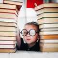 Cute little girl taking a book from top of books tower. Reading and kids education concept