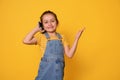 Cute little girl talks on mobile phone, smiles with beautiful toothy smile looking at camera, isolated yellow background Royalty Free Stock Photo