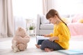 Cute little girl with teddy bear reading book on floor Royalty Free Stock Photo