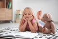 Cute little girl with teddy bear reading book on floor at home Royalty Free Stock Photo