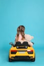 Cute little girl with toy bear driving children`s car on light blue background, back view Royalty Free Stock Photo