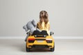 Cute little girl with toy elephant driving children`s car near grey wall indoors, back view Royalty Free Stock Photo