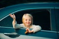 Cute little girl traveling in the car and observing nature from open window. Little girl waving hand for good bye in the Royalty Free Stock Photo