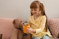 Cute little girl treating toy bear with cup of hot cocoa drink at home