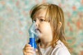 A cute little girl is undergoing medical inhalation treatment with a nebulizer at home. The girl is sitting and doing cough treatm Royalty Free Stock Photo
