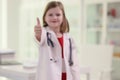 Cute little girl in uniform of medic shows thumb up gesture