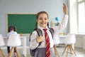 Cute girl in uniform raising hand, ready to answer her lesson at classroom. Portrait of adorable first grader at school Royalty Free Stock Photo