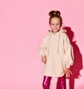 Cute little girl with updo posing with confident look in pale-pink sweatshirt and glossy leggings. Royalty Free Stock Photo