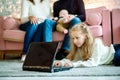 Cute little girl is using a digital tablet while lying on the floor at home, in the background her handsome father and mother with Royalty Free Stock Photo