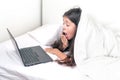 Cute little girl using a laptop in bed under a blanket. A girl is watching a cartoon on a laptop and yawns. Overwork at school. Royalty Free Stock Photo