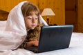 Cute little girl using a laptop in bed under a blanket Royalty Free Stock Photo