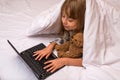 Cute little girl using a laptop in bed under a blanket Royalty Free Stock Photo