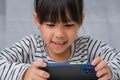 Cute little girl using smartphone and smiling while sitting at table in house. Happy Asian girl holding phone in hands, online Royalty Free Stock Photo