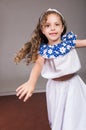 Cute little girl wearing beautiful white and blue dress with matching head band, actively posing for camera, studio Royalty Free Stock Photo