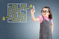 Cute little girl wearing business dress and finding the maze solution writing on the whiteboard. Blue background.
