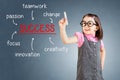 Cute little girl wearing business dress and writing success diagram on glass board with marker. Blue background.