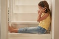 Cute little girl wearing headphones sitting on stairs at home and listening music Royalty Free Stock Photo