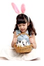 Cute little girl wearing pink bunny ears and holding rabbit in basket while sitting on white background. Joyful kid celebrating Royalty Free Stock Photo