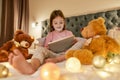 A cute little girl wearing pyjamas sitting alone on a huge bed barefoot enjoying her time watching cartoons on a tablet Royalty Free Stock Photo