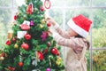 Cute little girl wearing a red Santa Claus hat. She is decorating the tree. Royalty Free Stock Photo