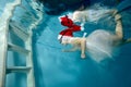 A cute little girl, wearing a Santa hat and a white dress, swims under the water to the white stairs in the children`s Royalty Free Stock Photo