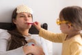 Cute little girl wearing uniform playing doctor or nurse with young mum or nanny in bedroom, checking mother throat Royalty Free Stock Photo